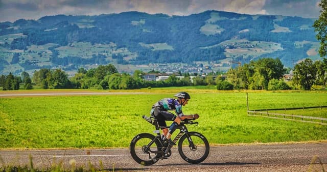 Christian Plesca riding the time trial bike past open fields with mountains behind.