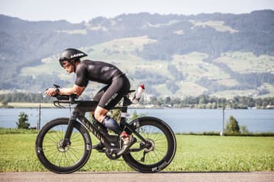 Christian Plesca on the time trial bike on a road beside a lake.